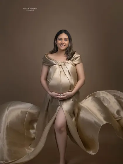 A full view of the golden goddess maternity look. The makeup is understated, complementing the dramatic and artistic styling of the photoshoot.
