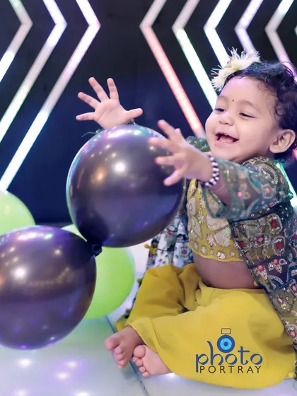 A joyful, candid shot of the birthday girl in a traditional yellow outfit, laughing as she plays with a balloon on a lit dance floor.