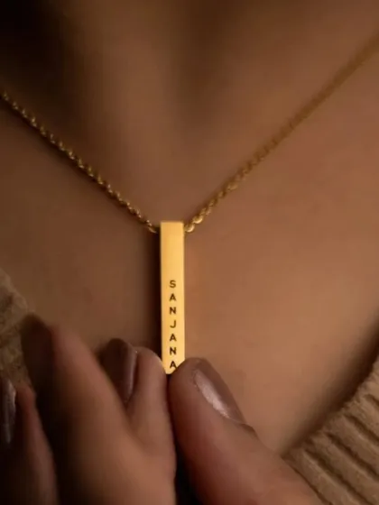 This close-up shows a gold bar pendant engraved with the name 'Sanjana'. The clean font and minimalist design make it a versatile piece, perfect for wearing alone or layering with other necklaces.
