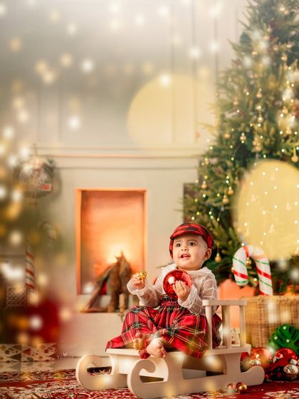 A magical, softly lit portrait of a baby in a sleigh, holding a Christmas ornament with beautiful bokeh lights in the background.
