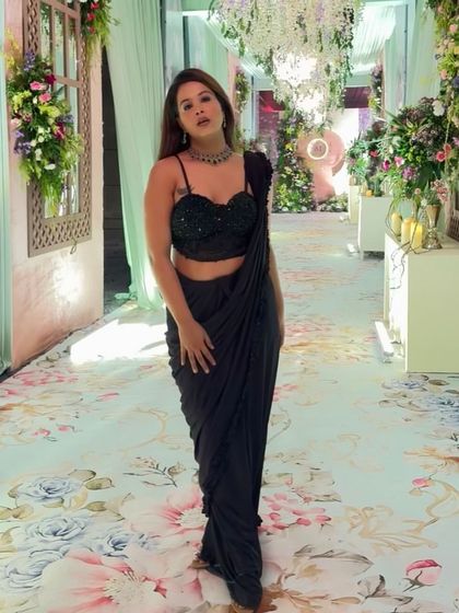 This black saree looks stunning against the floral decor of a wedding venue. It's a versatile piece that works for almost any formal occasion.