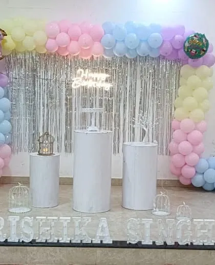 A pastel rainbow balloon arch with a silver tinsel curtain and white pedestals.