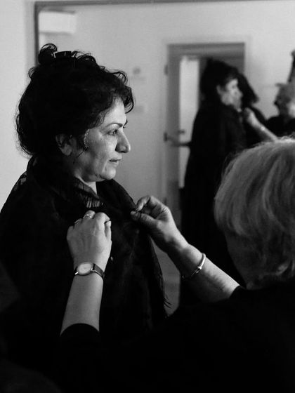 A costume designer makes adjustments to an actor's shawl during a fitting.