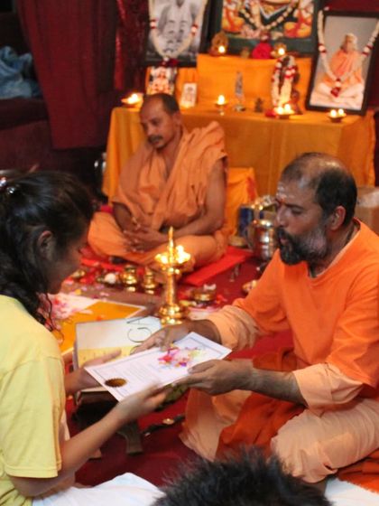 A student receives her certificate from a Swami during a traditional Guru Purnima ceremony, honoring the lineage of teachers.