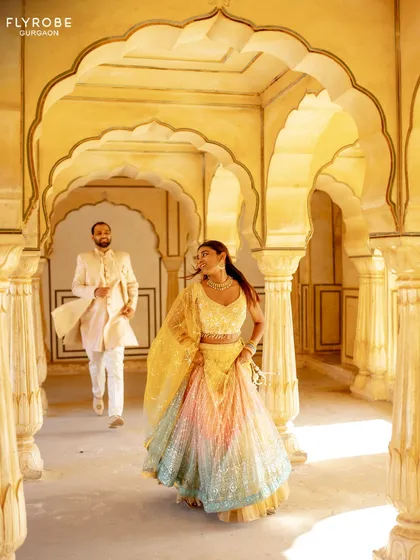 A playful and romantic shot from a pre-wedding shoot. Her multi-colored lehenga and his ivory sherwani look stunning against the architectural backdrop.