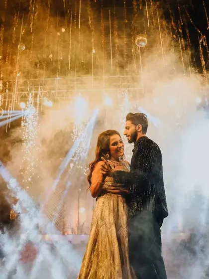 The magic of a Sangeet night. Hilesh and Ankita share a dance under a sky of golden lights and smoke, creating a truly cinematic moment.
