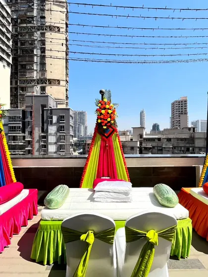 A colorful rooftop Haldi setup, with vibrant drapes and floral arrangements creating a festive atmosphere against the city skyline.