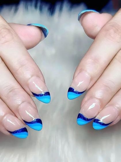 A creative take on the French manicure with wavy, layered blue tips in both solid and glitter polish on almond-shaped nails.