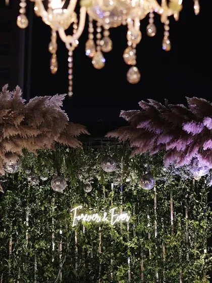 A close-up of the neon sign photo booth, showing the detail of the pampas grass and hanging crystals.
