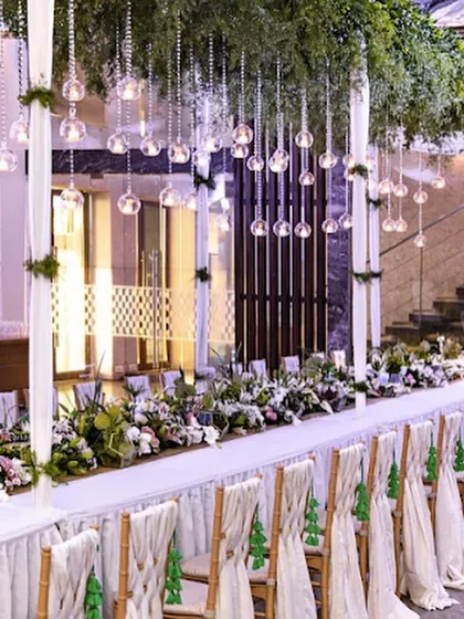 A long head table adorned with hanging glass baubles and a runner of fresh greenery. This unique and enchanting decor highlights our commitment to creating bespoke and unforgettable event designs.