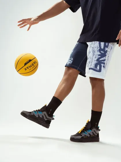 A detailed shot focusing on the brand's shorts and sneakers. By capturing the model interacting with a basketball, the image reinforces the sportswear theme and shows the product in its intended environment.