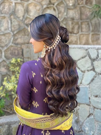 A beautiful half-up hairstyle with a floral bun and soft waves for a Mehendi look. The side passa adds a traditional touch to this modern and elegant style.