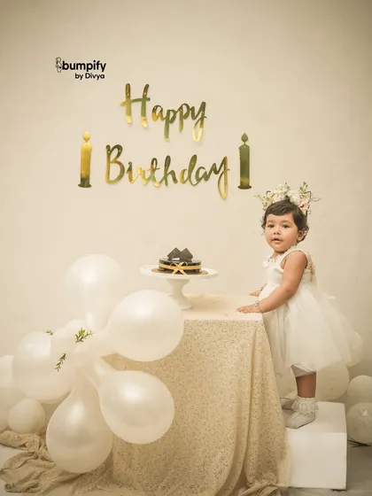 A full length portrait of the birthday girl in her beautiful white dress, standing by the cake table in our elegant studio setup.