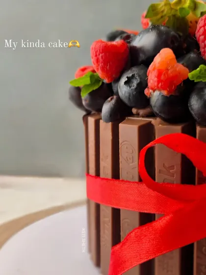 A side view of the KitKat cake, showing the crisp chocolate bars held together with a festive red ribbon. It's a cake that's as beautiful as it is delicious.