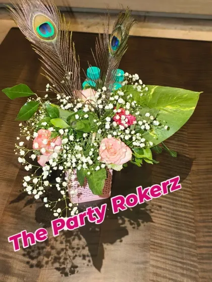 A small and delicate table centerpiece made with roses, baby's breath, and peacock feathers, perfect for a Teej party.