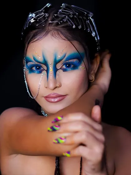 A fierce and powerful fantasy look, featuring bold blue face paint and a crown made of safety pins.