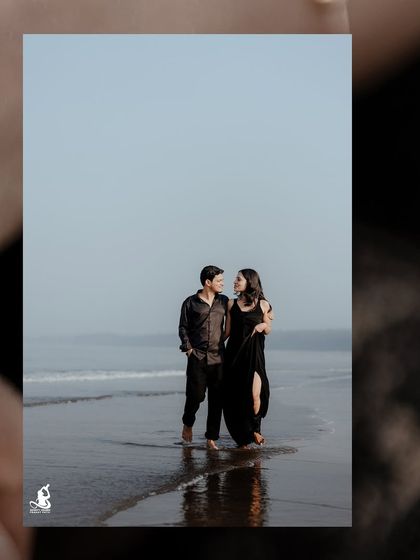 A simple, elegant shot of a couple walking barefoot on the wet sand, their dark outfits creating a striking visual against the light sky.