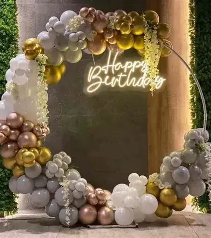 Our skills extend to all celebrations, like this elegant birthday party setup. The circular frame adorned with chrome gold, white, and rose gold balloons, complete with a neon 'Happy Birthday' sign, shows our ability to create chic and sophisticated decor.