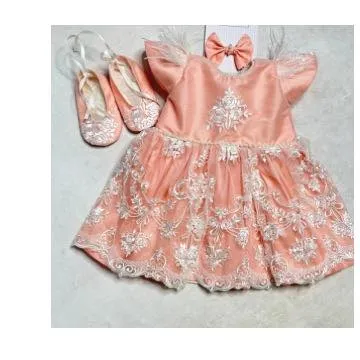 A beautiful newborn dress in peach, featuring delicate white lace embroidery and feather-capped sleeves. The set comes with matching soft booties and a hair bow.