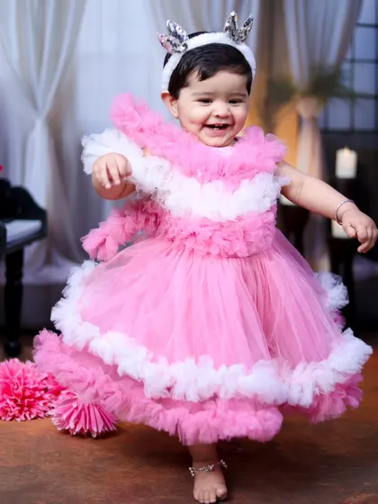 A joyful, dancing baby girl in a beautiful pink and white ruffled dress.