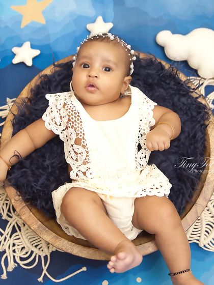 A peaceful sitter session with a celestial theme. The baby is nestled in a wooden bowl against a deep blue, starry backdrop, creating a 'love you to the moon and back' feel.