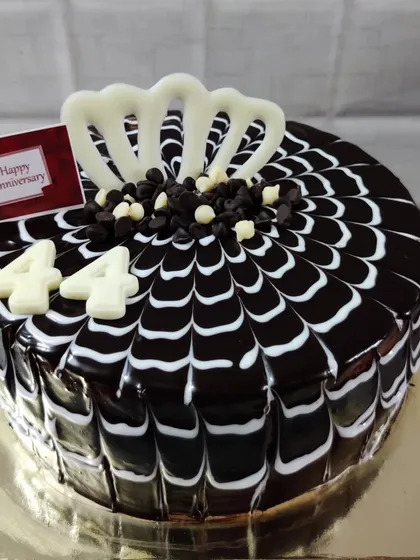 A chocolate truffle cake for a 44th anniversary. The spider-web glaze and white chocolate accents create a striking design.