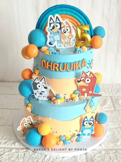 A fun and colorful two-tier cake for a fifth birthday, celebrating the popular show Bluey and Bingo. The design is decorated with edible character toppers and bright, playful chocolate spheres.