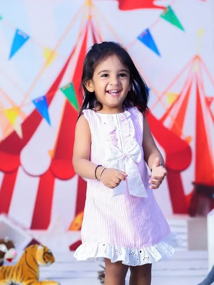 A happy two-year-old girl enjoying her carnival-themed birthday shoot. Her bright smile and the colorful circus tent backdrop create a festive atmosphere.