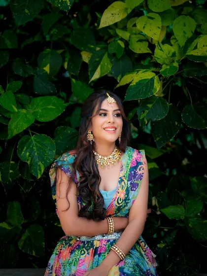 A candid shot of a model in a colorful Mehendi lehenga. The natural green background makes the vibrant outfit and her joyful expression the focus of the image.
