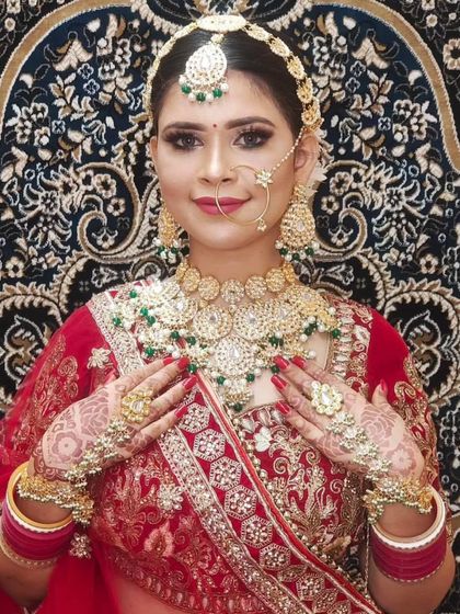 A happy bride in a red lehenga, showcasing her full jewellery set, including the hathphool and oversized rings. The smile says it all!