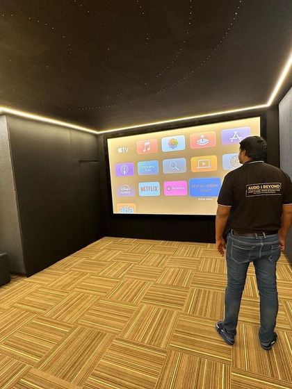 The project is nearing completion. Our technician inspects the finished room, which features beautiful wood-paneled acoustic walls and patterned flooring, ensuring every element of the home theater design is executed to perfection before final calibration.