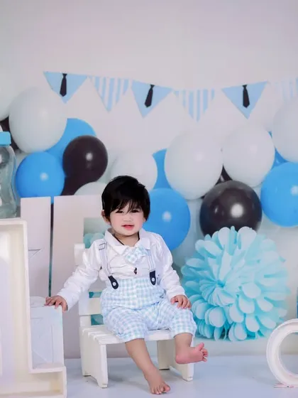 A dapper little gentleman celebrating his first birthday. He is sitting on a small white bench in a blue, white, and black themed setup.