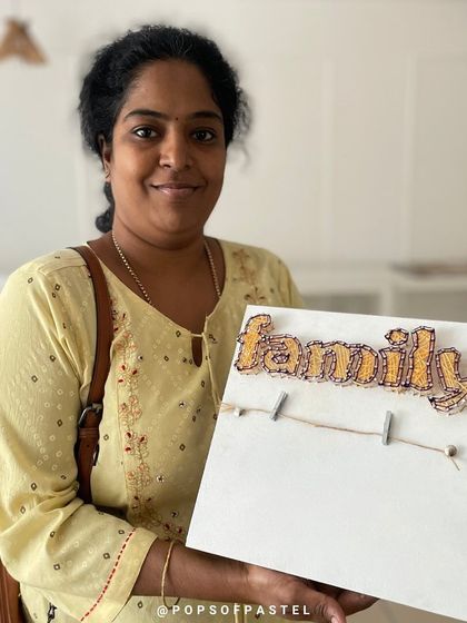 A proud participant holds up her completed "Family" string art photo holder, a perfect handmade piece for her home.