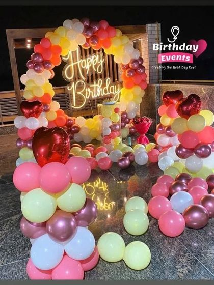 A vibrant outdoor setup on a terrace, using a warm palette of yellow, orange, pink, and rose gold balloons, complete with heart-shaped foil balloons.