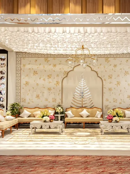 A full view of the white and gold lounge setup. The space is cohesive and luxurious, with a floral-patterned backdrop, intricately carved tables, and a beautiful ruffled fabric ceiling.