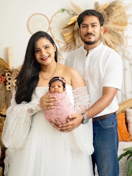 A beautiful first family portrait. The new parents are dressed in white, holding their precious newborn girl in a bright and airy boho setting.