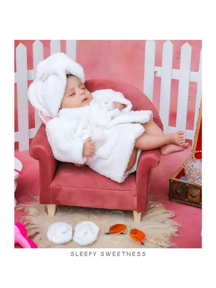 A wider view of the "spa day" setup, showing the baby sleeping peacefully in a pink chair surrounded by cute props.