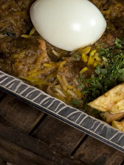A close-up on the corner of a biryani tray, showing the detail of the garnish and the texture of the slow-cooked meat and rice.