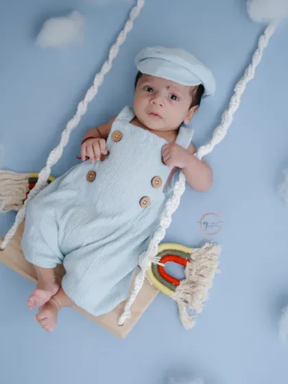 A full view of the dreamy sky setup, with a newborn in a cute newsboy cap resting on a swing among fluffy clouds.