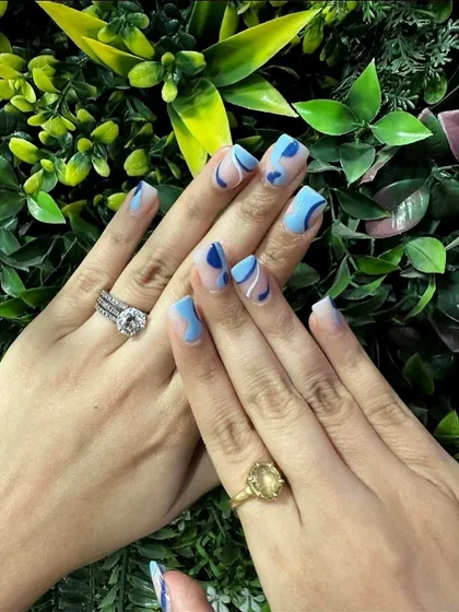An abstract blue manicure set against our signature green wall. This design uses different shades of blue on a neutral base to create a modern, artistic pattern on squared nails.