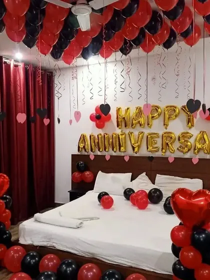 A bold and romantic anniversary decoration in red and black. The room is filled with balloons on the ceiling and floor, with "Happy Anniversary" foil balloons above the bed as the main feature.