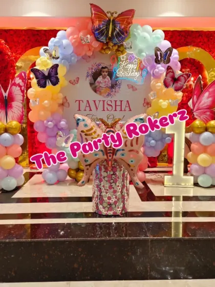 Another angle of the butterfly theme party, showing the main backdrop against a textured red wall. The setup includes a custom printed circular panel, pastel balloon decor, and large butterfly cutouts.