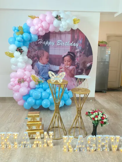 I also create beautiful setups for twins' birthdays. This decoration for Naan and Kashvi's birthday features a custom photo backdrop of the twins, surrounded by a pink and blue balloon arch and their names in marquee letters.