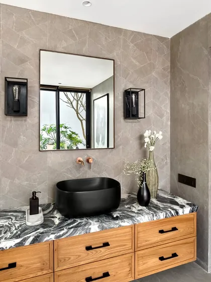 We used a striking black and white marble for the countertop in this bathroom, paired with a warm teak vanity. The design is a play of contrasts, with modern black fixtures set against textured grey walls and natural wood.