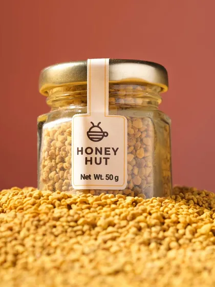 A close-up hero shot of a jar of bee pollen sitting on a mound of the product. This macro shot emphasizes the texture and natural quality of the ingredient.