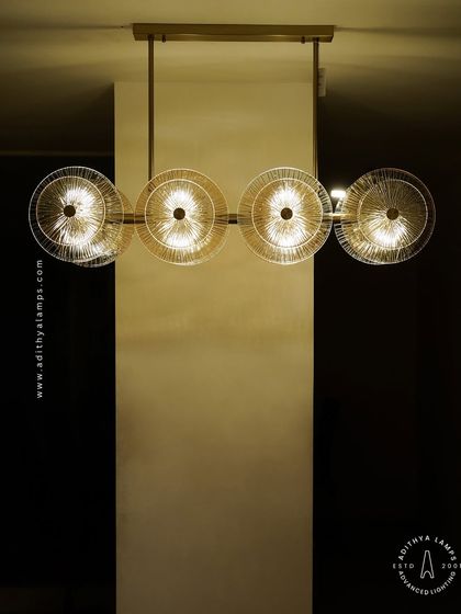 A linear chandelier featuring an arrangement of clear and amber-tinted textured glass discs. This fixture provides both direct and ambient light, adding a layer of sophistication and warmth to dining areas and boardrooms.