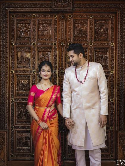 A formal portrait of the couple holding hands against a beautifully carved wooden door, symbolizing the new door they are opening in their lives.