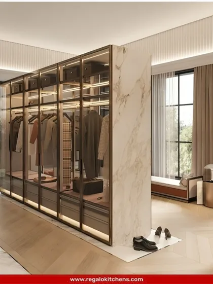 This freestanding glass wardrobe acts as a room divider, creating a distinct dressing area without closing it off completely. The marble accent wall adds a touch of luxury.