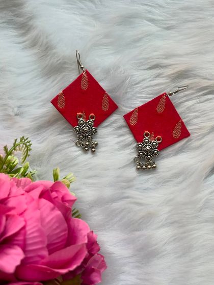 Handmade red fabric earrings with a delicate gold print and a small oxidised silver flower charm.