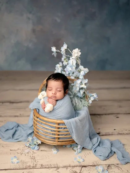 Sweet dreams with a tiny teddy. This close-up captures the peacefulness of a newborn, holding a small bear, in a basket of blue.